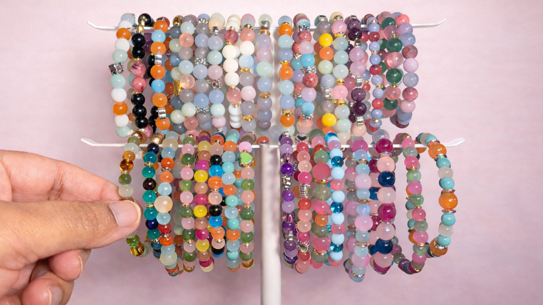 Adult hand selecting a colorful beaded bracelet from a display, showing a variety of glass and natural stone bracelets suitable for girls, with stackable designs arranged for everyday and school-appropriate wear