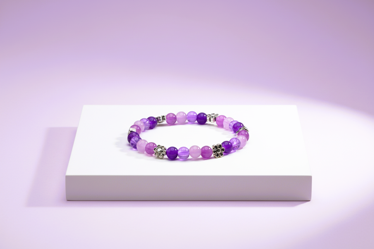 Handmade beaded bracelet with purple glass beads silver floral spacers displayed on a white pedestal against a soft lavender background