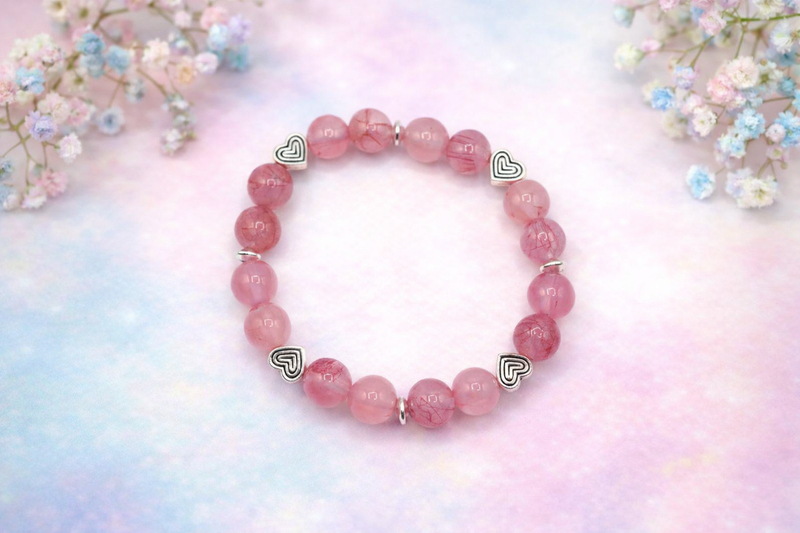 Handmade bracelet with natural gemstone pink jade beads heart charms on a soft, background with aesthetic flowers