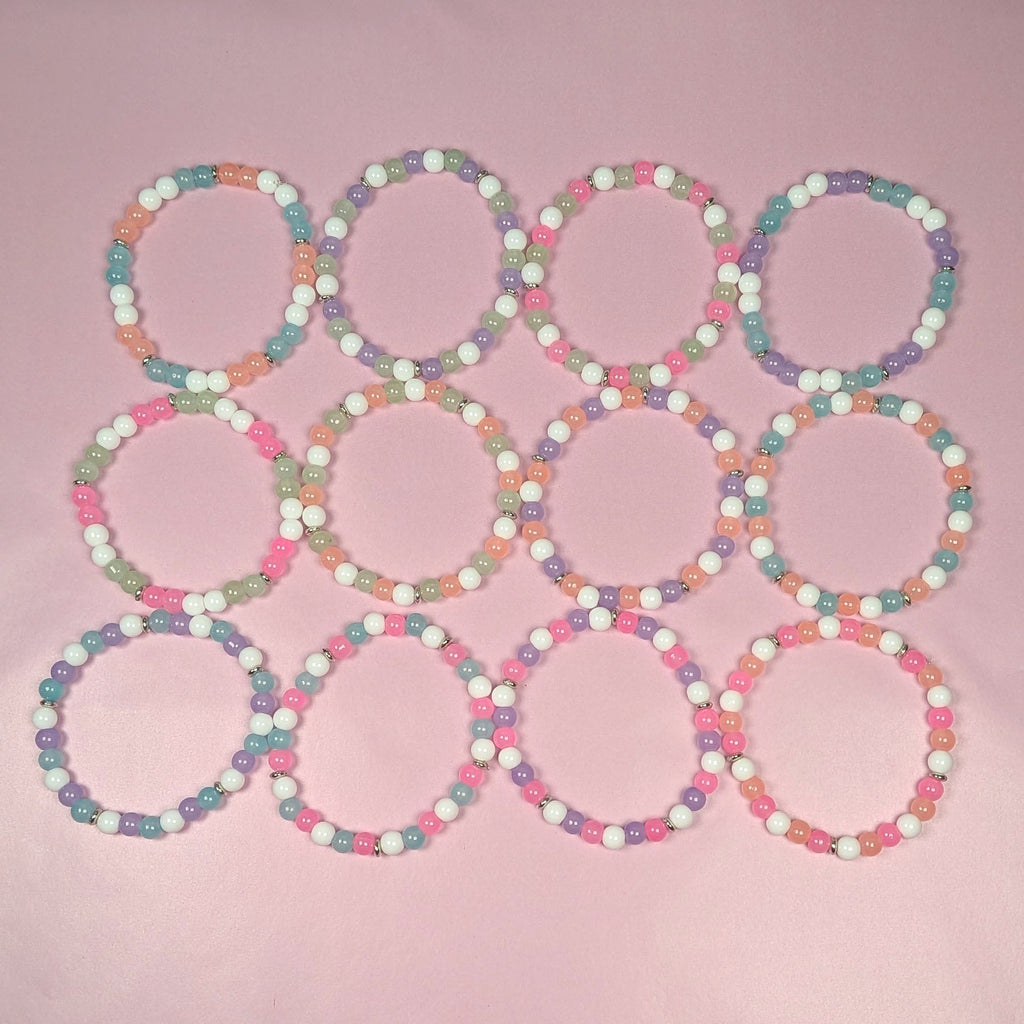 12-piece pastel glass bead bracelet party favor set arranged in grid layout, 6mm stretch bracelets in pink, peach, mint, aqua, lavender and white for kids