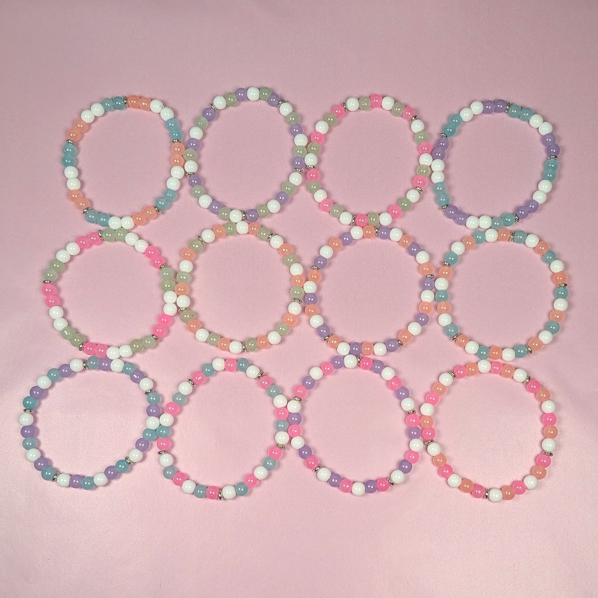 12-piece pastel glass bead bracelet party favor set arranged in grid layout, 6mm stretch bracelets in pink, peach, mint, aqua, lavender and white for kids