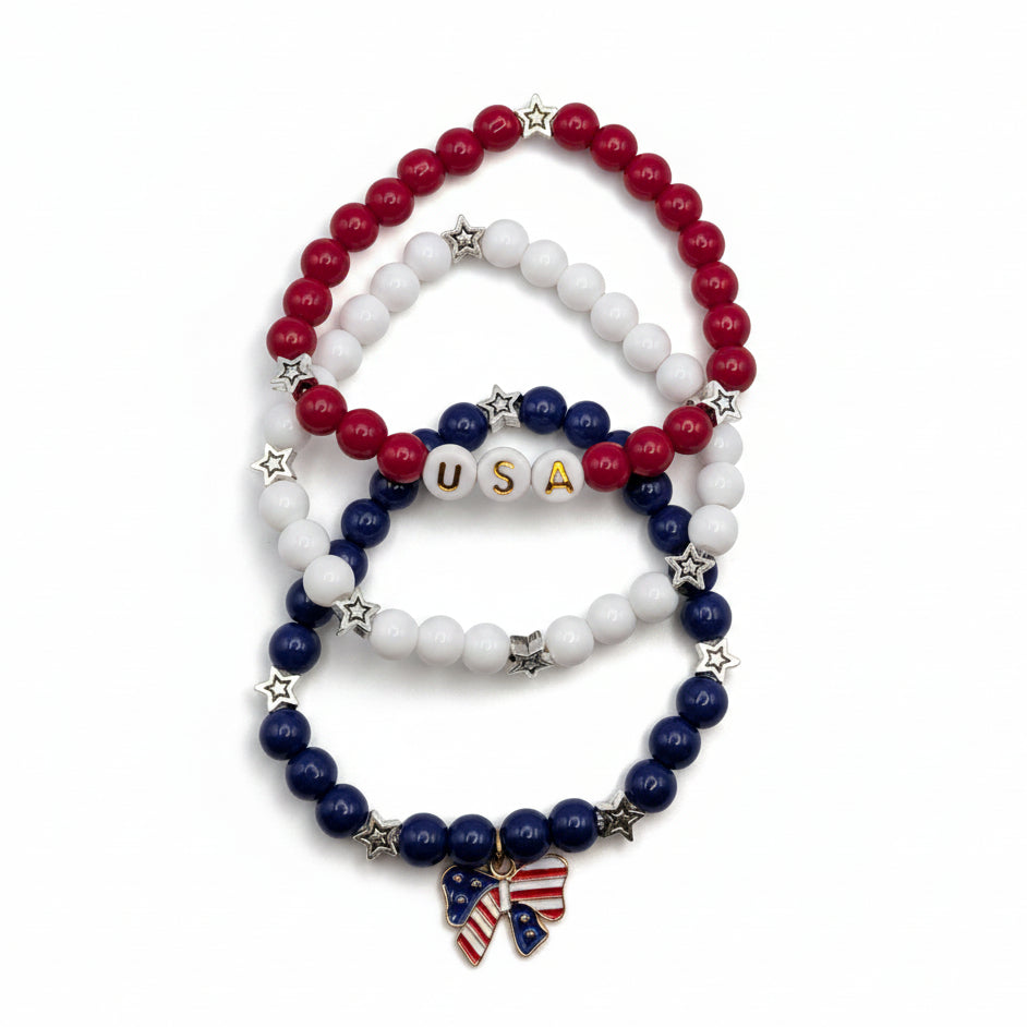 Three-piece patriotic bracelet set with red, white, and blue 6mm glass beads, star accents, USA letter beads, and an American flag bow charm arranged together